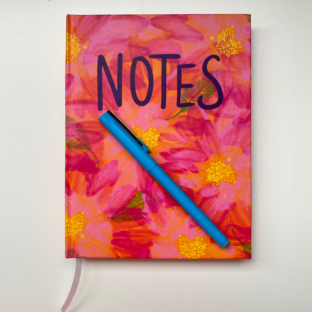 Bright pink and orange painterly flowers with yellow centers on the cover of a lined journal, with the word 